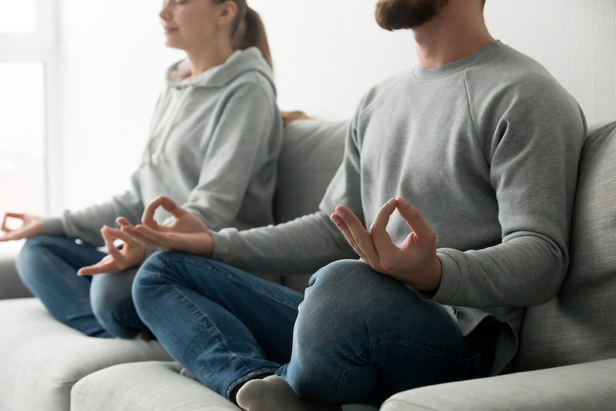 couple-meditating-practicing-yoga-home-sofa-focus-hands (1)